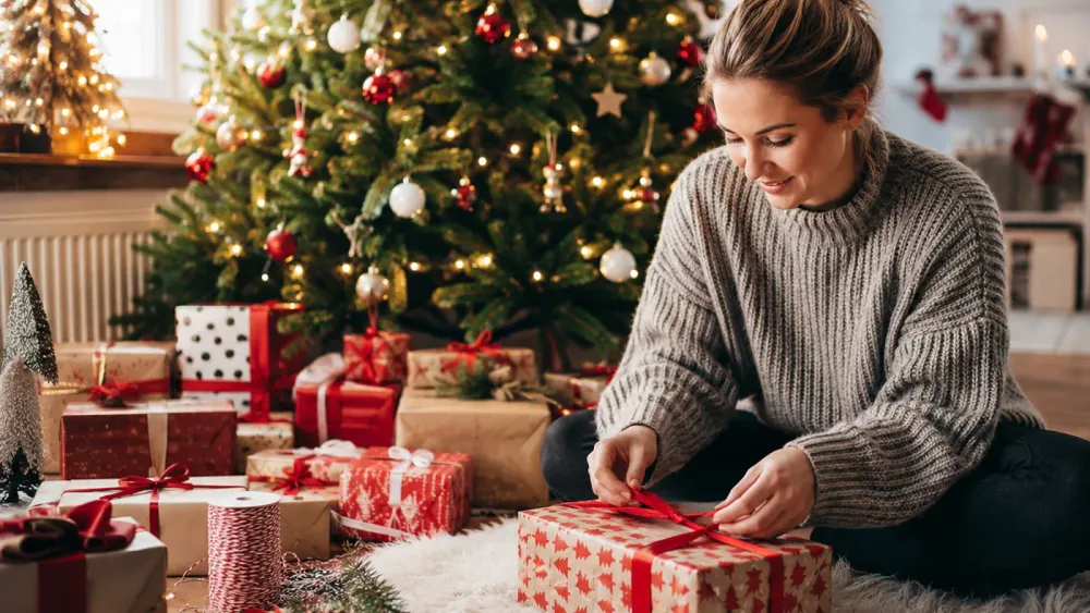 Frau verpackt Weihnachtsgeschenke vor dem geschmückten Weihnachtsbaum
